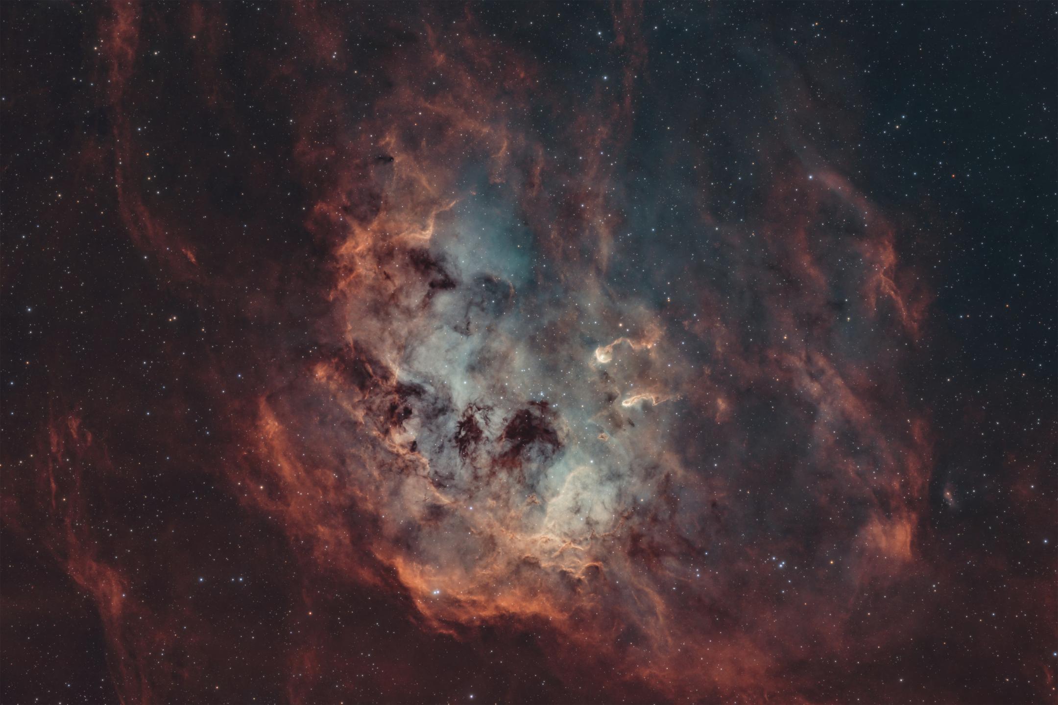 A rounded cloud of rust-orange emission wrapped around a pale blue-green interior, cut through by dark dust lanes, with two small bright knots near the centre trailing tails that point away from it.