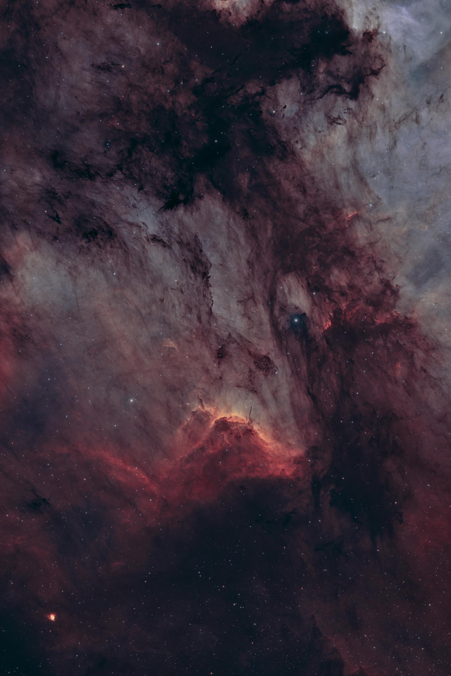 A close view of a glowing ridge of red-orange gas running diagonally across the lower half of the frame, with ragged dark dust columns pressing down on it from above.