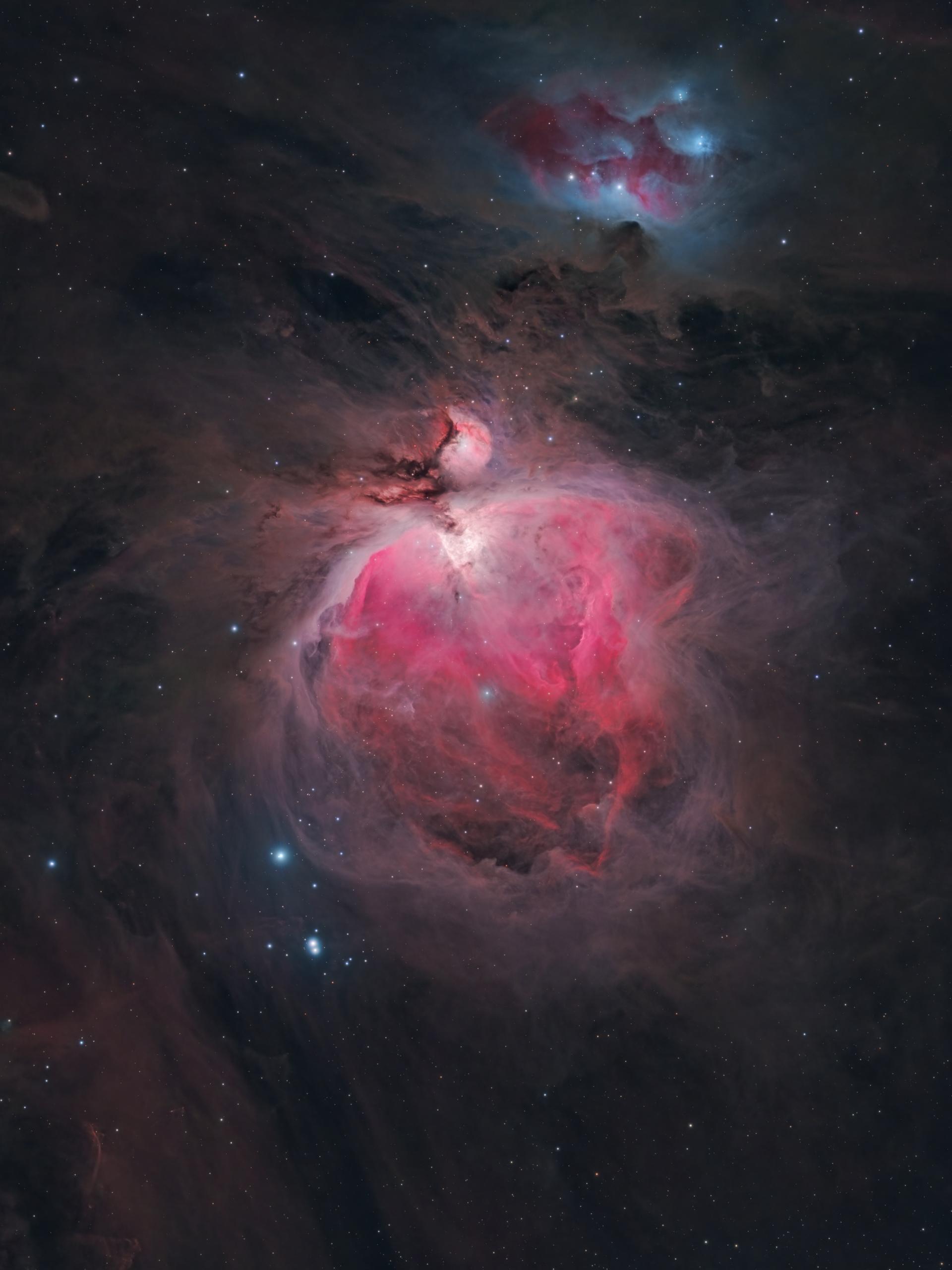 A bright rose-pink nebula with a searing white core, its wings sweeping outward into darker folded dust; a smaller patch of blue and red nebulosity sits above it, and a short line of blue-white stars runs below.