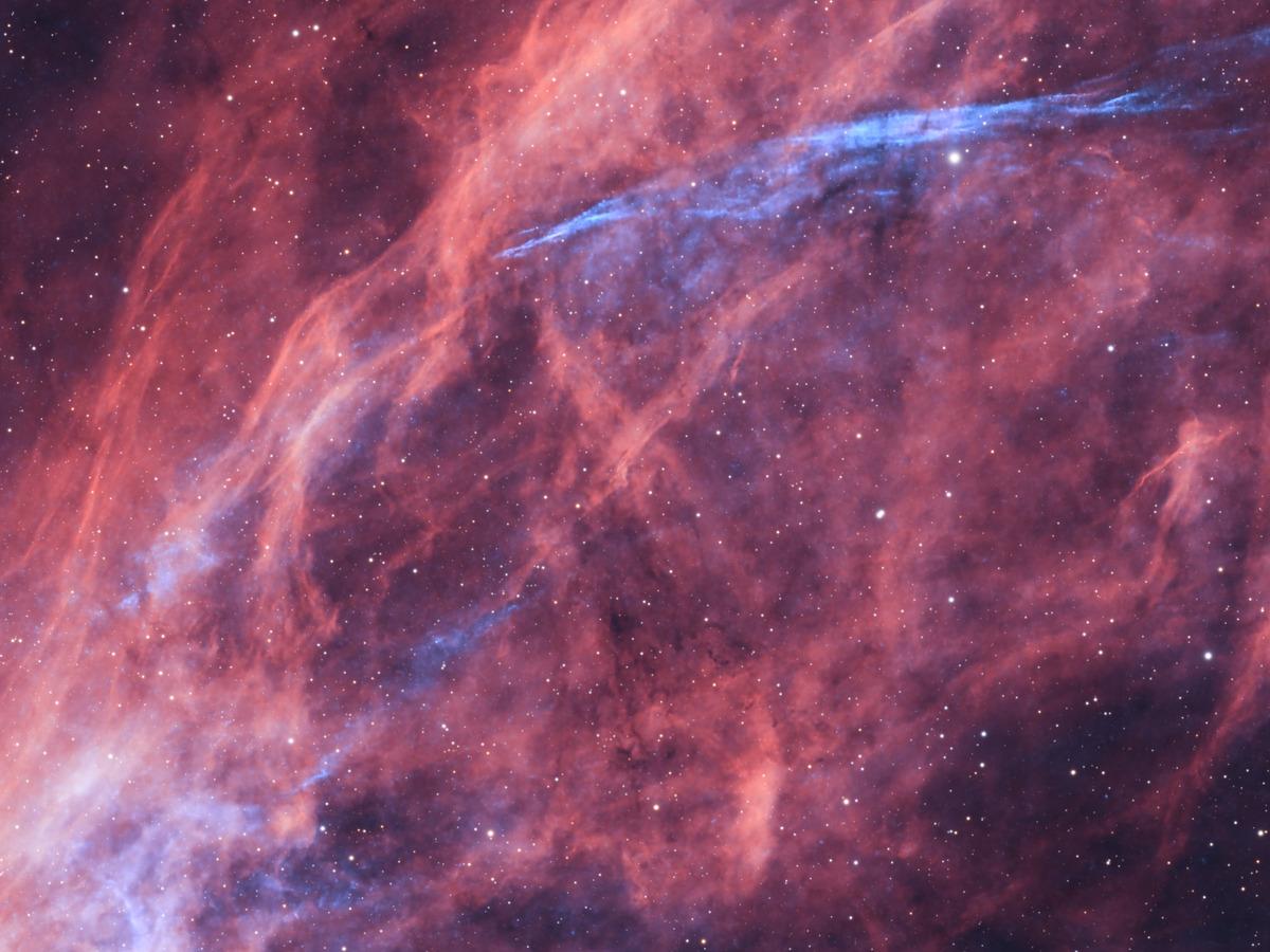 Close-up of the faint blue OIII filaments of the W63 supernova remnant, threading through the unrelated red foreground nebulosity